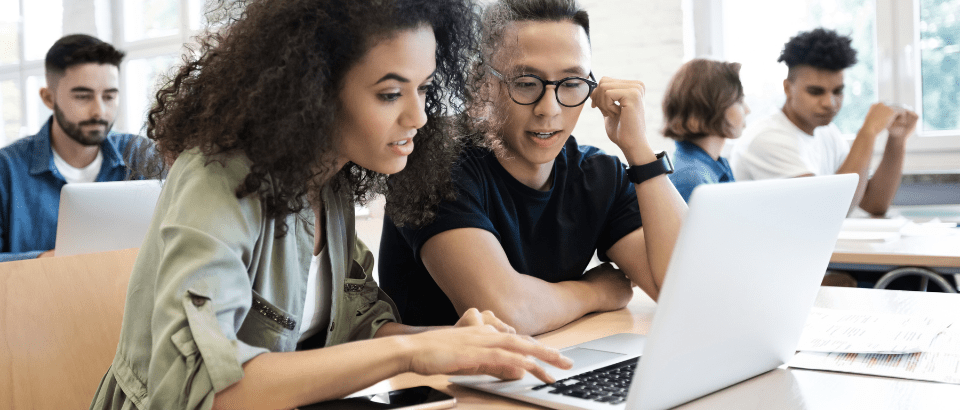 Two people sitting at a desk looking at a laptop screen together